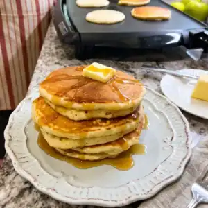 Stack of thick, fluffy Queen Elizabeth pancakes topped with butter and maple syrup